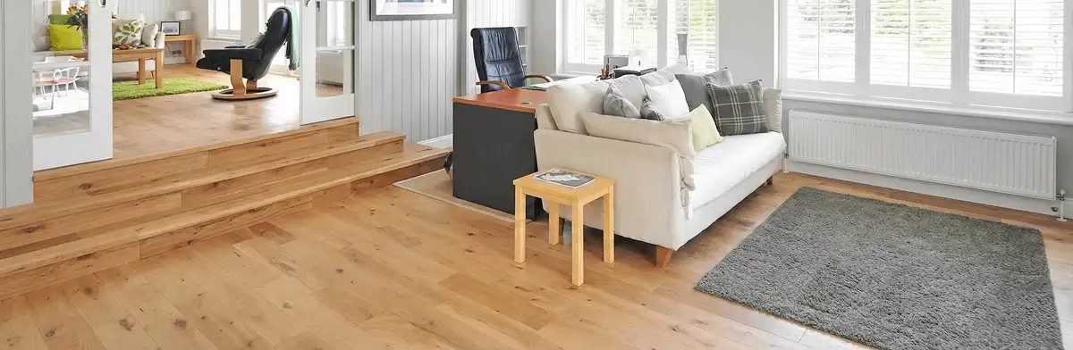 A modern living room with professionally installed laminate flooring, a beige sofa, a small side table, a gray rug, and large windows with white shutters in San Francisco, CA
